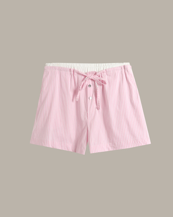 Pink and white vertically striped shorts with a white elastic waistband, drawstring tie, and front button closure, shown flat on a solid taupe background.