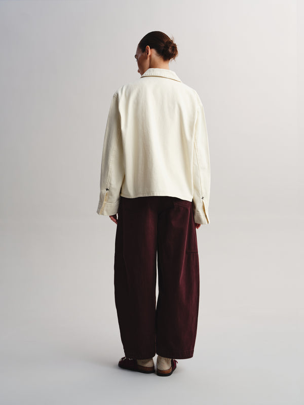 A model shown from the back wearing a cream-colored long-sleeve collared shirt and dark burgundy wide-leg trousers, standing against a light gray studio background.