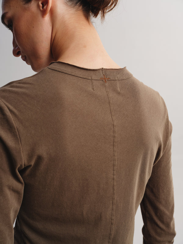 Close-up back view of a person wearing a brown ribbed long-sleeve top against a light gray studio background.