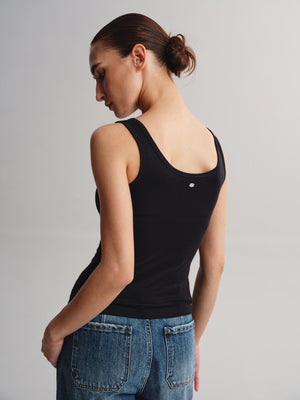 A woman shown from the back wearing a fitted black ribbed tank top and blue jeans against a plain light gray studio background.