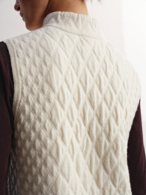 Close-up back view of a person wearing a quilted cream-colored sleeveless vest over a dark plum long-sleeve top.