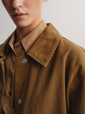 Close-up of a person wearing a brown corduroy overshirt over a tan collared shirt, showing the collar, buttons, and textured fabric against a plain light background.
