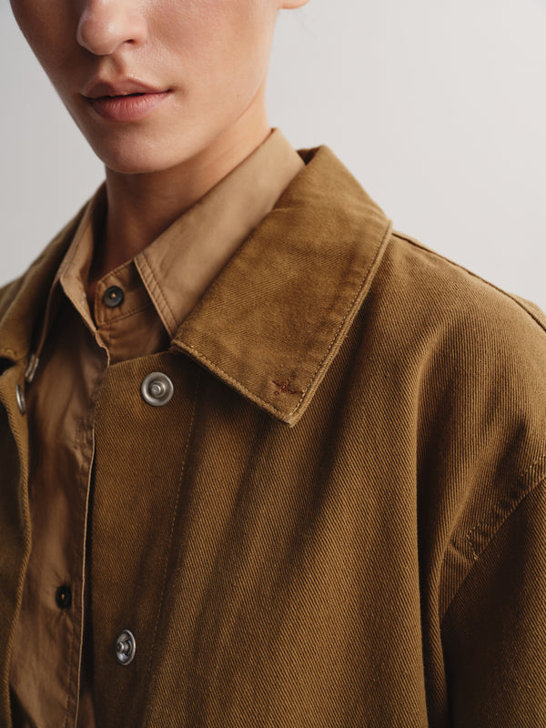 Close-up of a person wearing a brown corduroy overshirt over a tan collared shirt, showing the collar, buttons, and textured fabric against a plain light background.