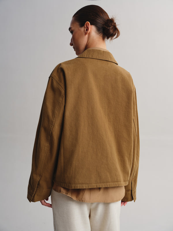 A model shown from the back wearing a brown corduroy jacket over a beige shirt and cream trousers, set against a plain light gray studio background.
