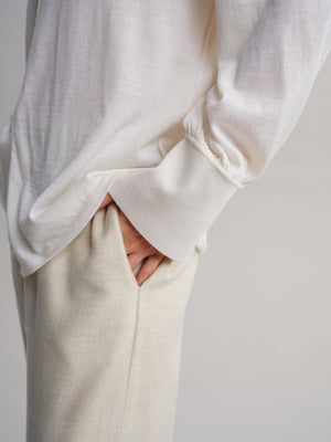 Close-up of a person wearing a loose white long-sleeve top and light beige trousers, with one hand tucked into a pocket.