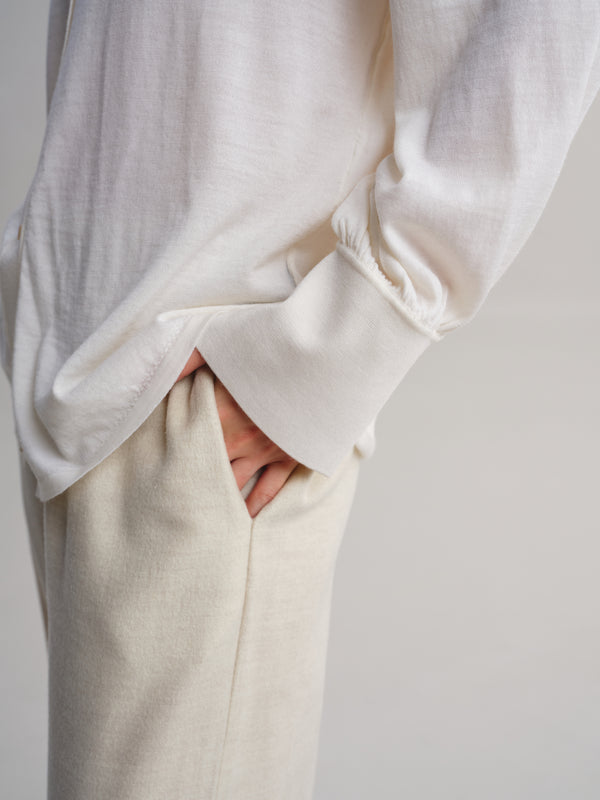 Close-up of a person wearing a loose white long-sleeve top and light beige trousers, with one hand tucked into a pocket.