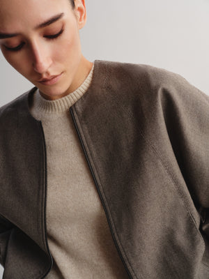 Close-up of a model wearing a taupe-brown wool-blend jacket over a beige ribbed knit sweater, set against a plain light gray background.