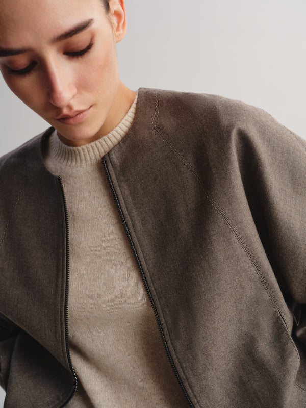 Close-up of a model wearing a taupe-brown wool-blend jacket over a beige ribbed knit sweater, set against a plain light gray background.