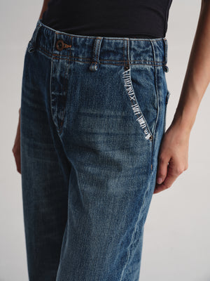 Close-up of a person wearing blue denim jeans with a black top, showing the side pocket detail and front waistband against a plain light background.