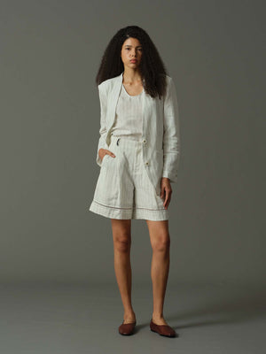 Woman wearing a light-colored outfit with shorts and a jacket on a gray background