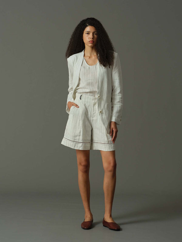 Woman wearing a light-colored outfit with shorts and a jacket on a gray background