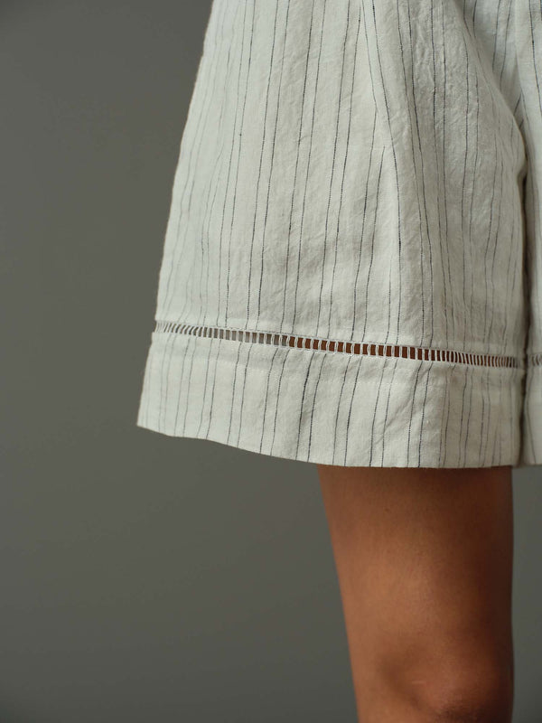 Close-up of a person wearing light-colored shorts with a subtle pattern on a plain background