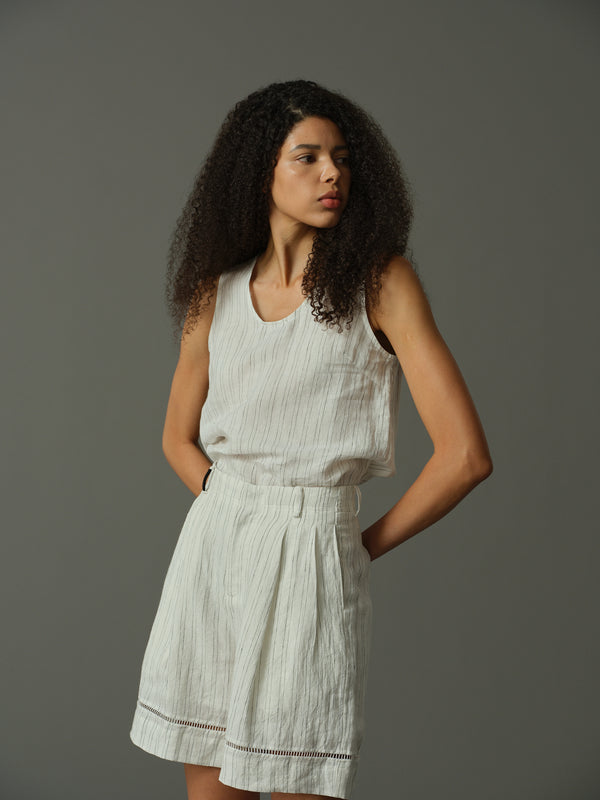 Woman wearing a light-colored sleeveless top and shorts against a gray background