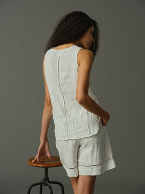 Woman wearing a light-colored sleeveless top and shorts against a gray background