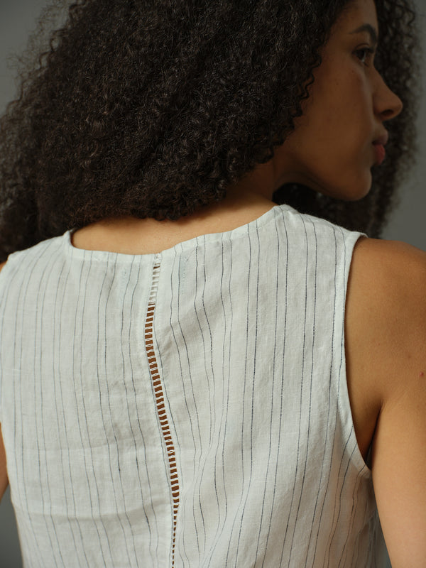 Woman wearing a light-colored sleeveless top with a subtle pattern.