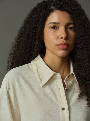 Woman wearing a light-colored shirt with a collar against a neutral background