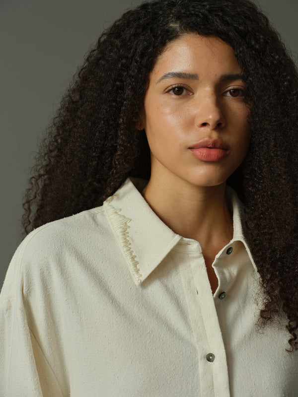 Woman wearing a light-colored shirt with a collar against a neutral background
