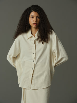 Woman wearing a beige shirt and pants against a gray background
