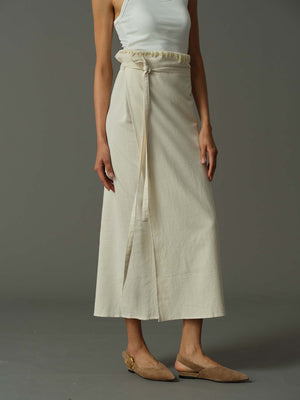 Person wearing a white top and beige wrap skirt on a gray background