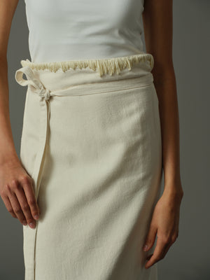 Person wearing a white top and cream-colored skirt against a gray background