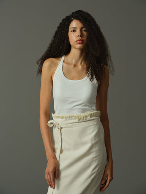 Woman wearing a white tank top and cream pants against a gray background