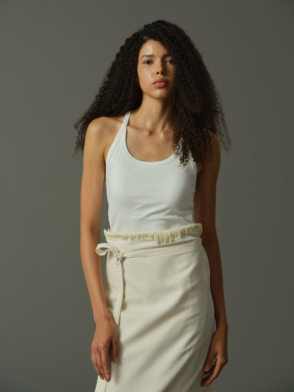 Woman wearing a white tank top and cream pants against a gray background