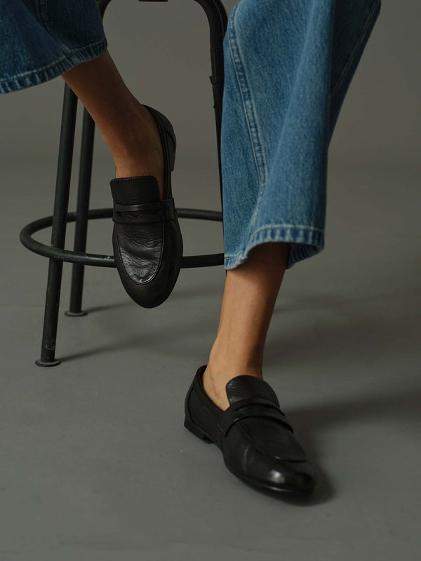 model wearing a pair of black loafers on a rustic wooden block