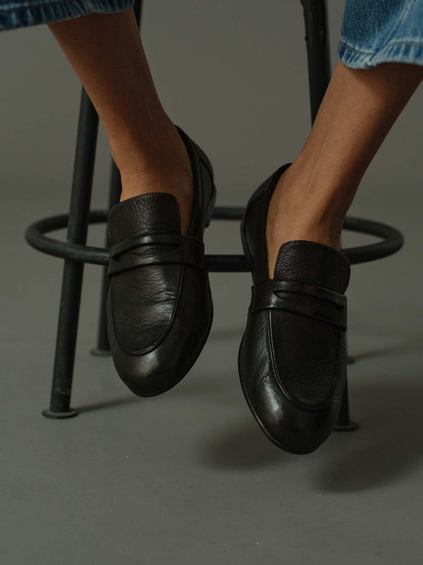 model wearing a pair of black loafers on a rustic wooden block