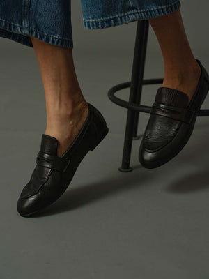 model wearing a pair of black loafers on a rustic wooden block