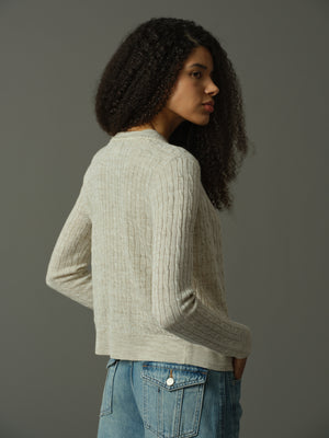 Woman wearing a khaki ribbed sweater and blue jeans against a gray background