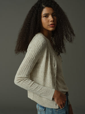 Woman wearing a khaki cable knit sweater against a dark background