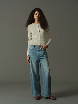 Woman wearing a khaki cardigan and blue jeans against a gray background