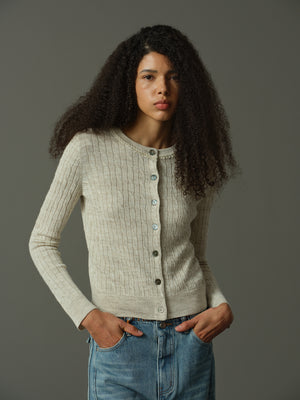 Woman wearing a khaki knitted cardigan and blue jeans against a gray background