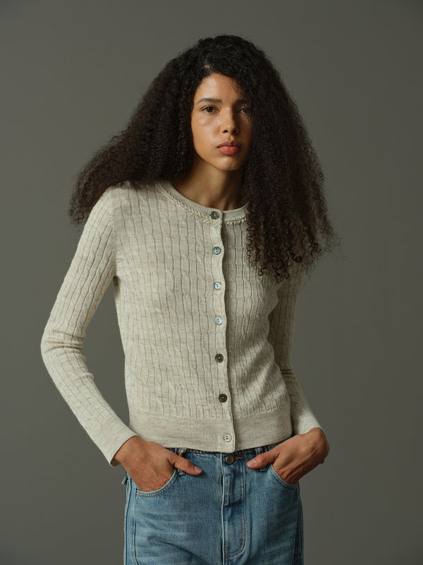 Woman wearing a khaki knitted cardigan and blue jeans against a gray background