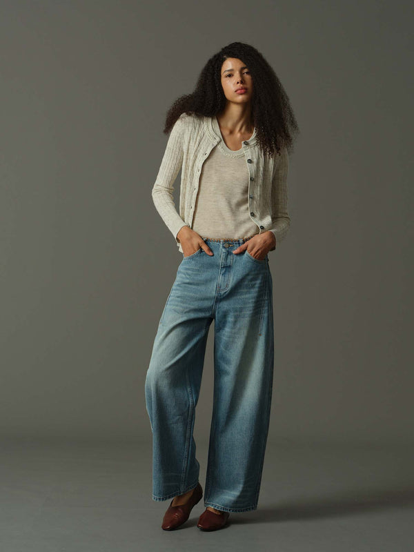 Woman wearing a khaki cardigan, khaki sweater, and blue jeans against a gray background