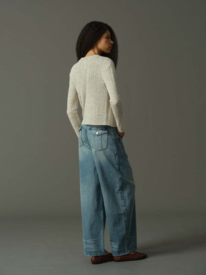 Woman wearing a light sweater and blue jeans against a gray background