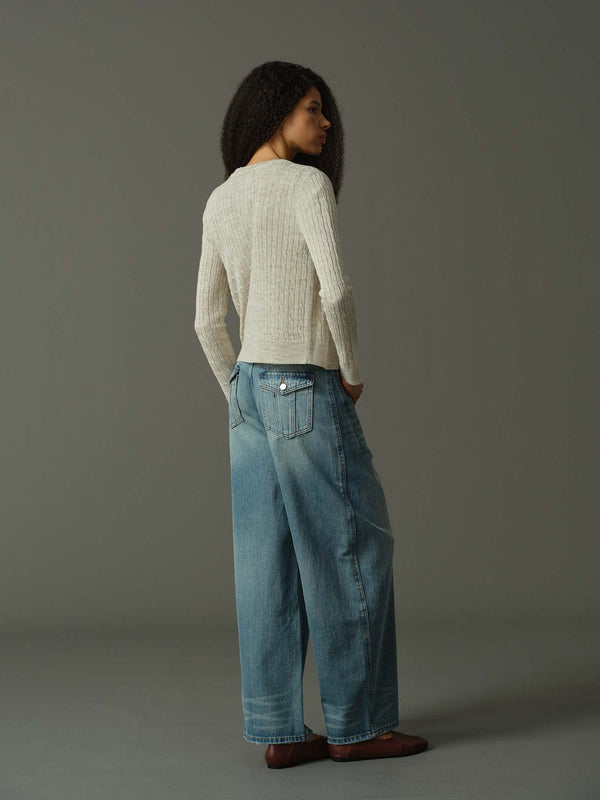 Woman wearing a light sweater and blue jeans against a gray background