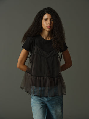 model wearing a black layered outfit with sheer cami and black t shirt underneath against a gray background