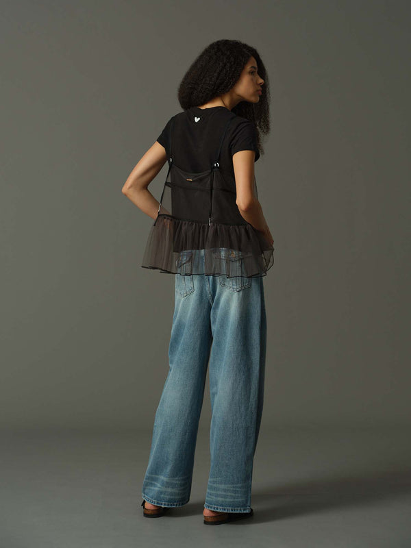 model wearing a black layered outfit with sheer cami and black t shirt underneath and blue jeans against a gray background