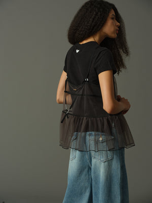 model wearing a black layered outfit with sheer cami and black t shirt underneath against a gray background