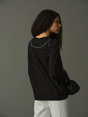 Woman wearing a black long-sleeve top with decorative elements on a gray background