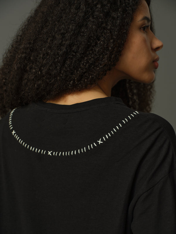 Person wearing a black top with decorative stitching on the back against a gray background