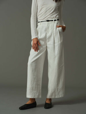 Person wearing white wide-leg pants and a light-colored top on a gray background