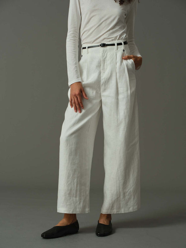 Person wearing white wide-leg pants and a light-colored top on a gray background