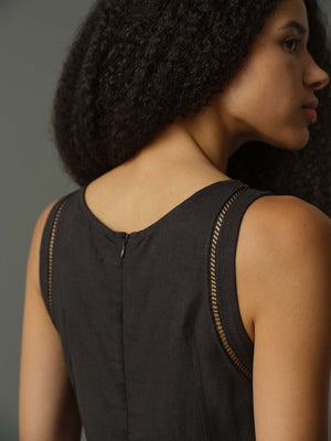 Woman wearing a black sleeveless top with gold trim on a gray background
