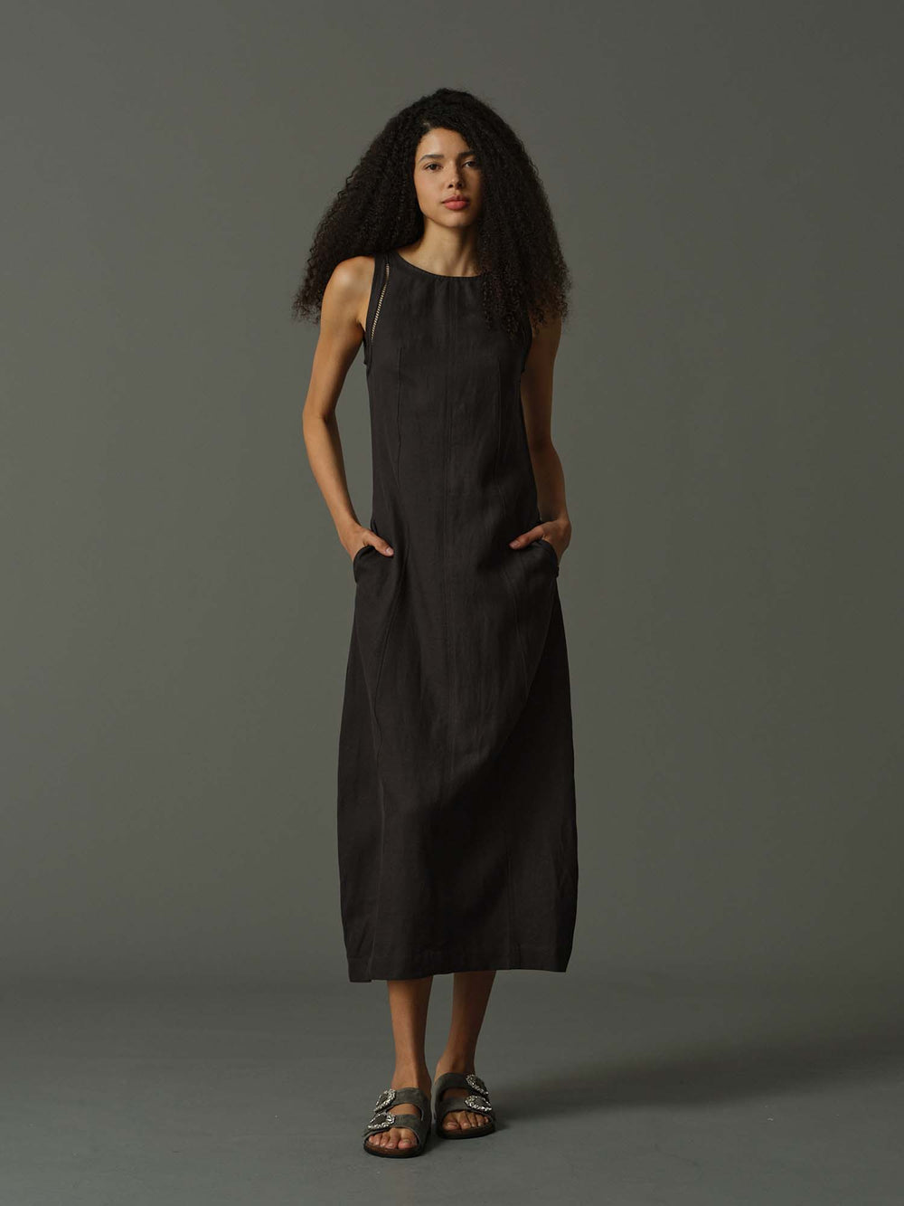 Woman wearing a dark grey sleeveless dress against a gray background
