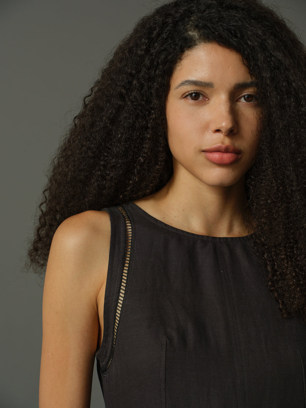 Woman wearing a dark grey sleeveless dress against a gray background