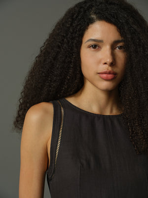 Woman with curly hair wearing a black sleeveless top against a gray background