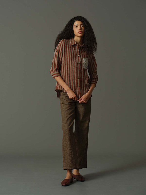 Woman wearing a striped shirt and brown pants against a gray background