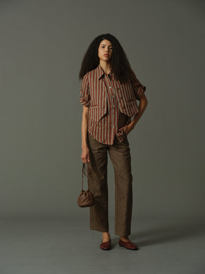 Woman wearing a striped shirt and brown pants holding a bag against a gray background